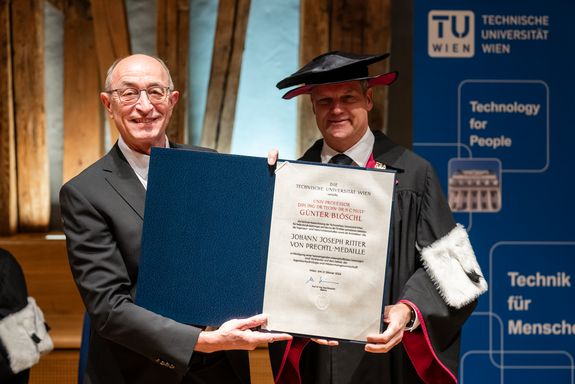 Günter Blöschl hält die Urkunde in Händen, neben ihm Rektor Jens Schneider