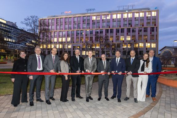 Gruppe von Personen vor einem Gebäude schneidet ein rotes Band durch.
