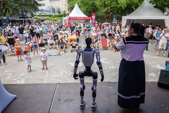 Frau mir Roboter auf Bühne. Vor der Bühne eine große Menschenmenge.