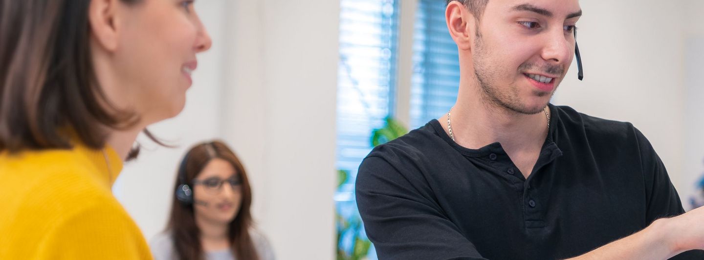 eine junge Dame blickt auf einen jungen Mann der auf einen Monitor zeigt