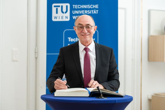 Günter Blöschl lächelnd an einem Pult, vor ihm ein dickes Buch