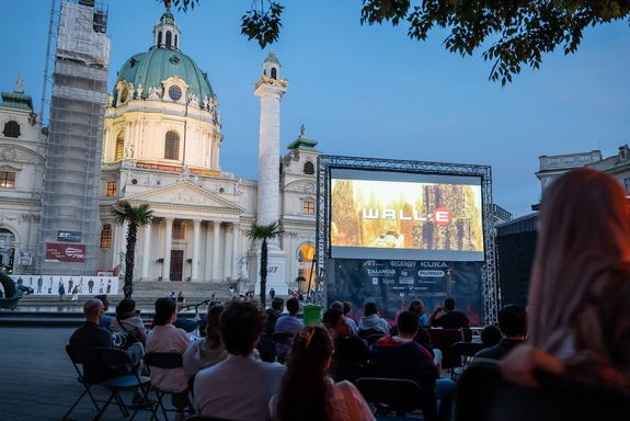 Kirche am Karlsplatz, Dämmerung, eine Leinwand auf der "WALL-E" steht und eine Vielzahl von Menschen