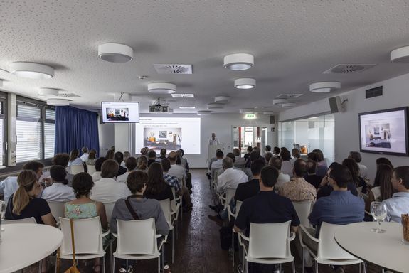 Raum mit menschen sitzen (Rücken zur Kamera), Sprecher bei Podium mit Mikro