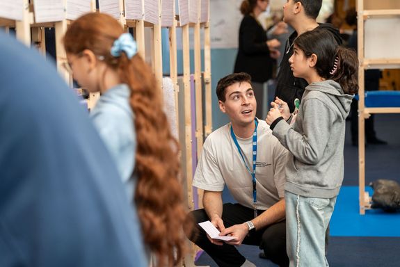 Kinder in der Austellung. groß im Bild Studierender erklärt Schülerin Station