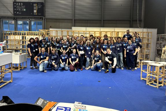 Gruppenfoto auf Messestand, davor Teppich in blau und Rennauto
