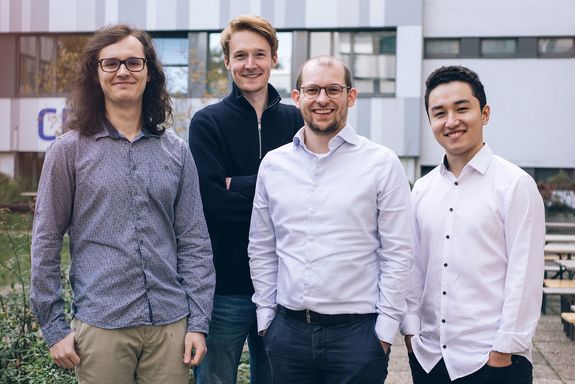 Group photo of four men in shirts, with a house facade in the background