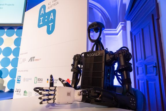 Schwarzer humanoider Roboter von NEOALP sitzt an einem Tisch