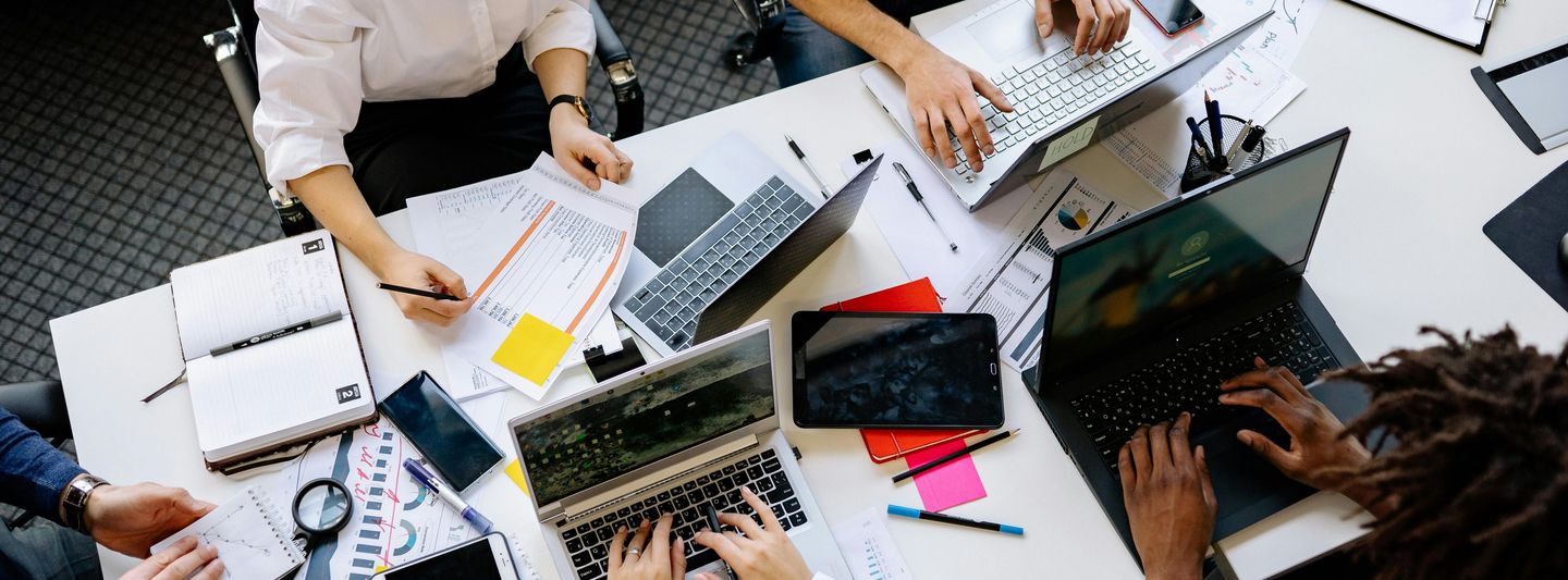 5 Arbeitende mit Notebooks an unordentlichen Bürotisch