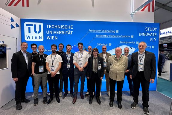 Gruppenfoto von mehreren Personen vor einem blauen Hintergrund mit großem TU-Logo