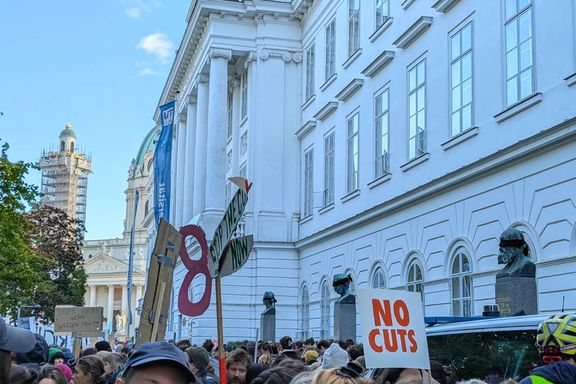 Hauptgebäude der TU Wien, davor Menschenmassen mit Plakaten und Bannern. Eines daovn eine Schere auf der steht: Stop the cut now.