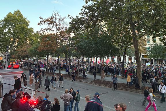 Demozug trifft vor der Uni Wien ein. Dicht gedrängte Personen marschieren hinter eine Reihe von Bäumen die Straße entlang.